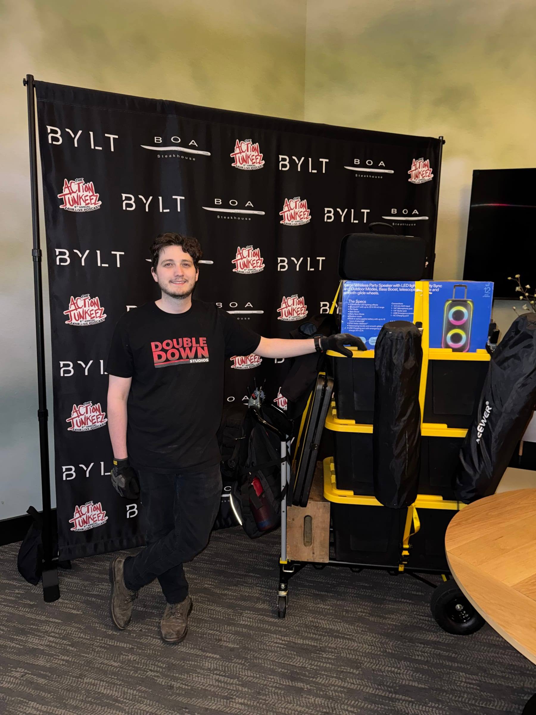 Travis Flesher with the kit beside a sponsor backdrop before an event recording